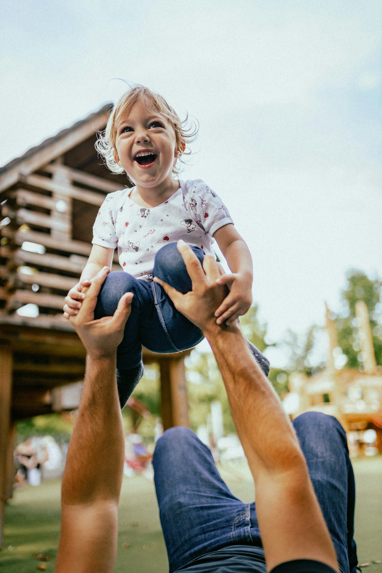 A parent outdoors carrying their young child on their shoulders, both smiling